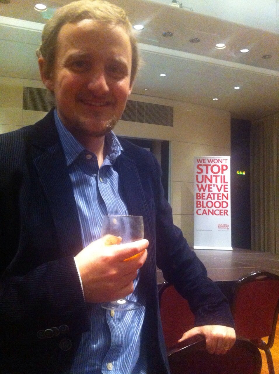 George, with LLR 'We won't stop until we've beaten blood cancer' poster in background