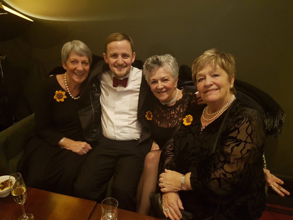 George on a sofa with three of the original Calendar Girls, wearing sunflowers