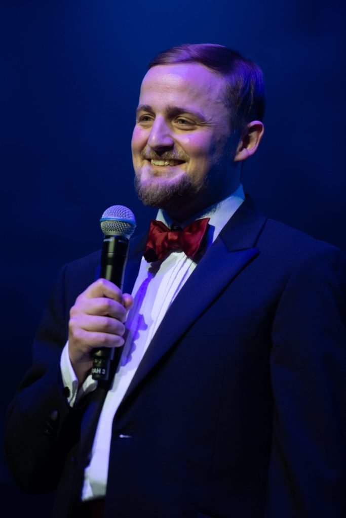 George looking content in tuxedo, holding a microphone
