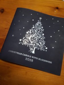 Bloodwise with the Stars 2018 programme cover: silver Christmas tree drawing with stars, on black background